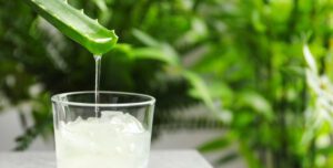 Aloe vera juice dripping from leaf into glass on table against blurred background with space for text